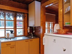 A compact kitchen with wooden cabinets, a white refrigerator, and a window with lace curtains.