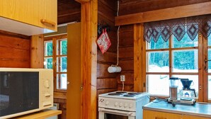 Ein rustikales Blockhaus-Interieur mit Holzwänden, einem Herd, einer Mikrowelle und einem Fenster mit Blick auf Bäume.