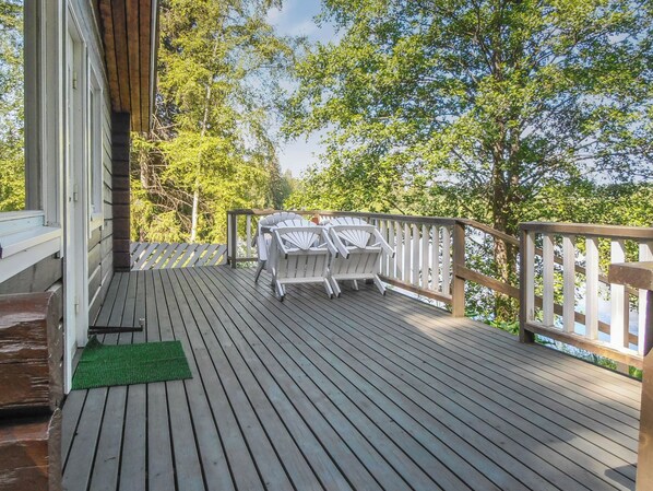 A wooden deck with a table and chairs, a green doormat, and a view of trees and sky.