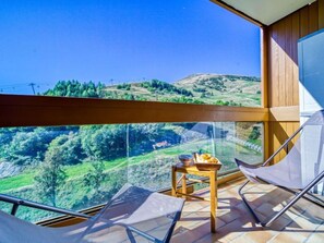 Un balcon offrant une vue dégagée sur un paysage montagneux, une petite table en bois avec un panier de pain et deux chaises.