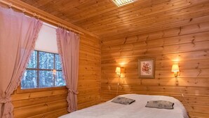 A cozy wooden cabin room with a bed, two wall-mounted lamps, a window with curtains, and a radiator. - Suvituuli by Interhome (Punkaharju)