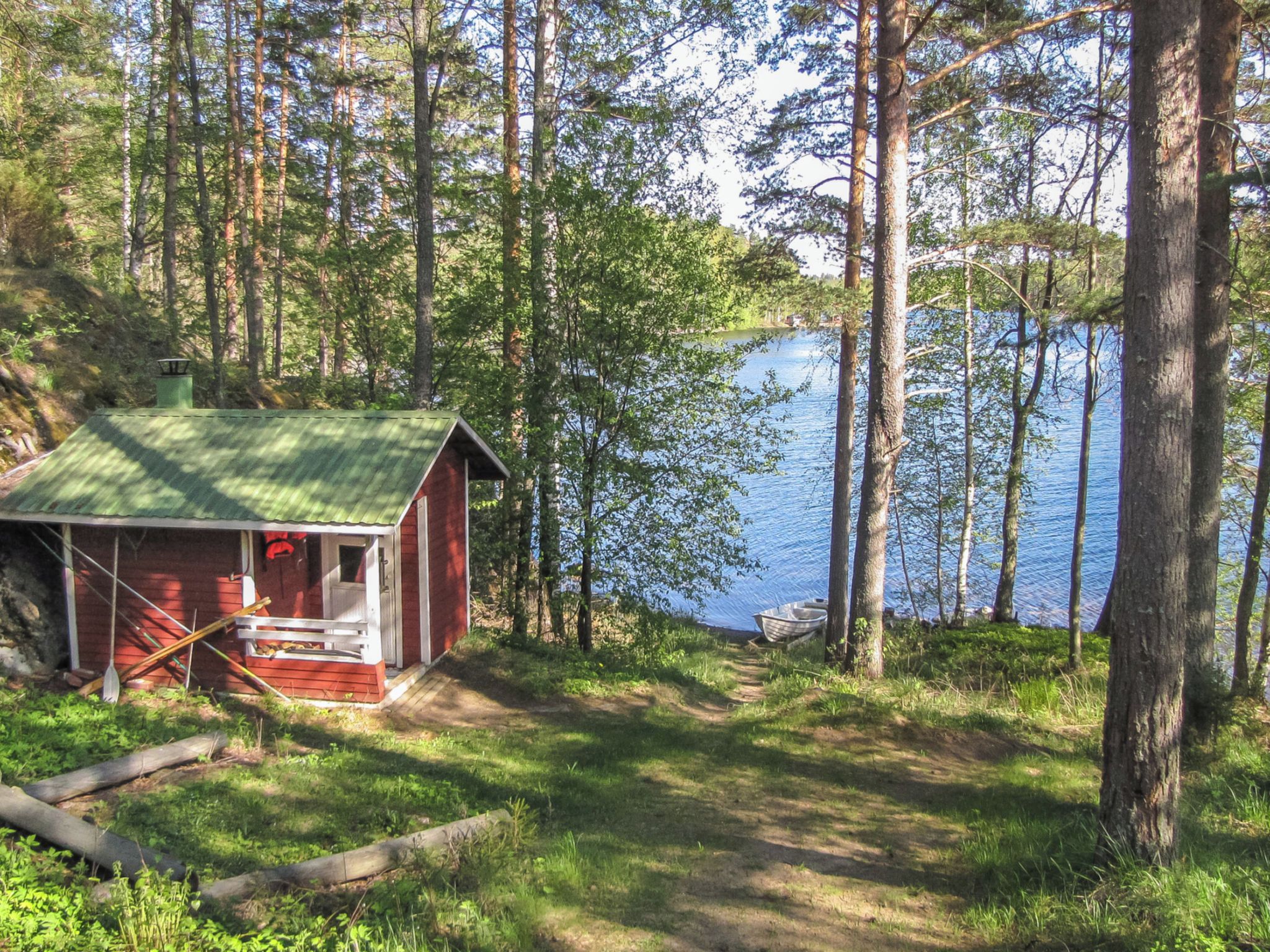 A cabin with a green roof, surrounded by trees and a lake.