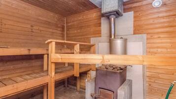 A sauna room with wooden benches, a sauna heater, and a stone wall.