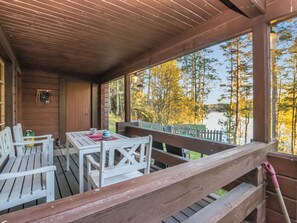A covered outdoor seating area with a table and chairs, overlooking a body of water and trees.