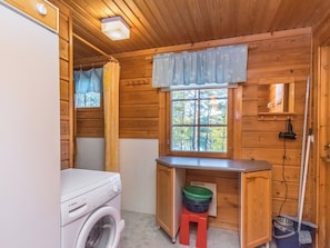 A compact wooden cabin with a washing machine, a small desk, and a window with a view of trees. - Suvituuli by Interhome (Punkaharju)
