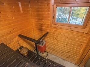 A wooden cabin interior with a window, a metal stove, and a wooden bench.