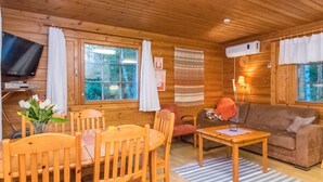 A cozy cabin interior with wooden walls, a dining table with chairs, a sofa, and a television on a shelf. - Suvituuli by Interhome (Punkaharju)