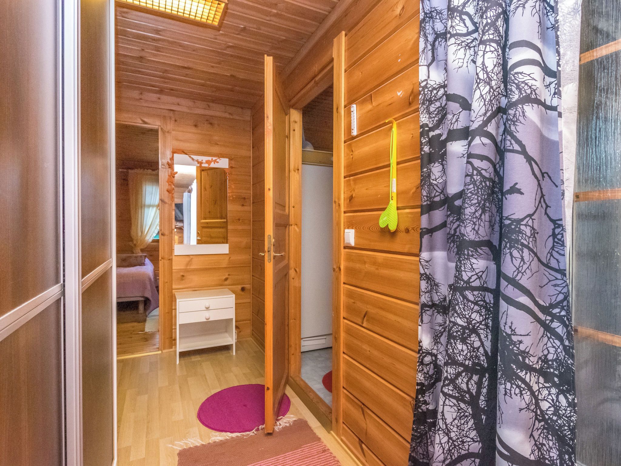 Ein Holzinterieur mit einem Bett, einem Nachttisch, einem Spiegel und einer Tür zu einem anderen Raum.