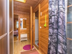 A wooden interior with a bed, a nightstand, a mirror, and a door leading to another room.