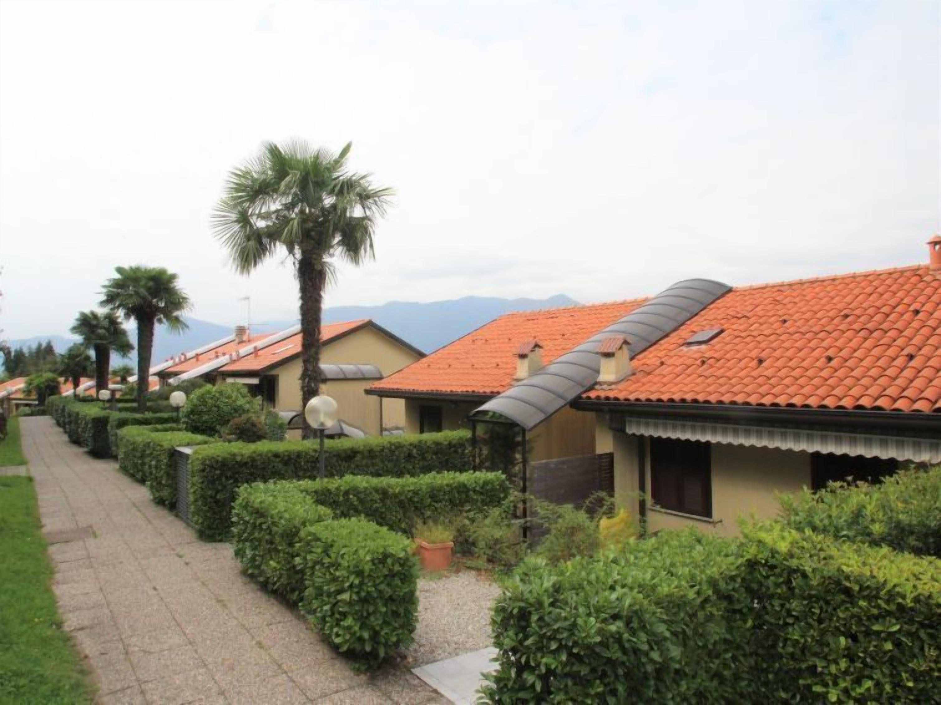 A row of Mediterranean-style villas with terracotta roofs, neatly trimmed hedges, and a paved walkway.