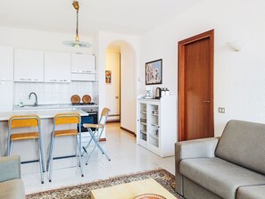 A modern kitchen with white cabinets, a dining area with yellow chairs, a grey sofa, and a wooden door.