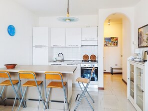 A modern kitchen with white cabinets, a gas stove, and a dining area with foldable chairs.