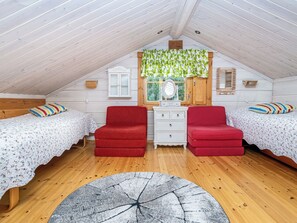 Ein gemütliches Schlafzimmer im Dachgeschoss mit zwei Einzelbetten, einem Schminktisch und einem roten Sessel.