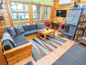 A cozy cabin interior with a sectional sofa, a wooden coffee table, a fireplace, and large windows offering a view of a snowy landscape. - Rukaniemen kontio by Interhome (Kuusamo)