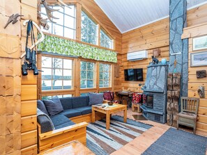 Ein Holzblockhaus-Interieur mit einer Couch, einem Kamin und einem großen Fenster mit Blick auf eine verschneite Landschaft.