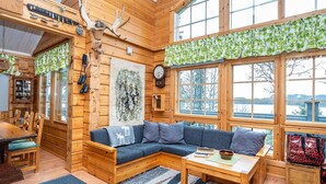 A cozy cabin interior with a wooden floor, a sectional sofa, a dining table, and large windows offering a view of the outdoors. - Rukaniemen kontio by Interhome (Kuusamo)