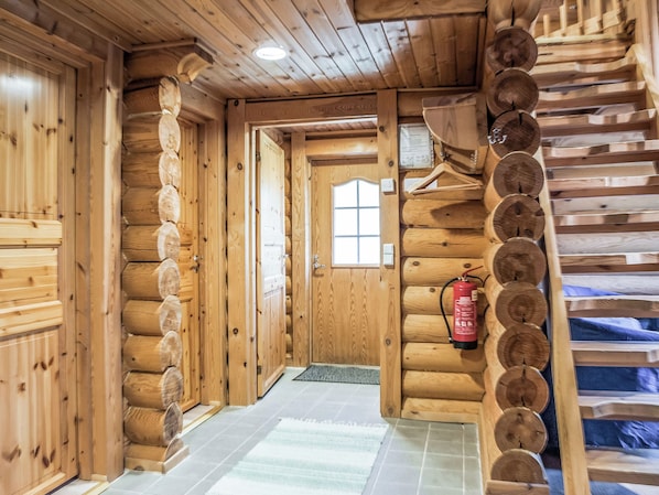 A log cabin interior with a wooden door, a fire extinguisher, and a window.