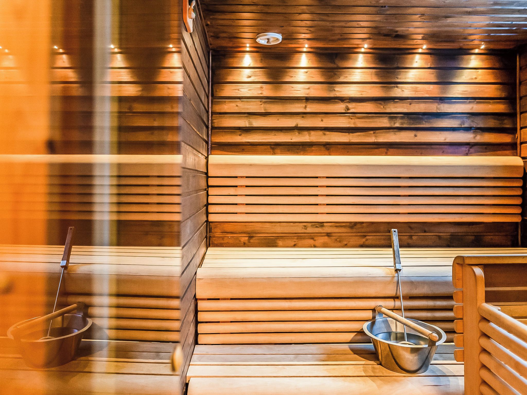 A sauna with wooden walls and benches, a metal bucket, and a wooden bench with a metal handle.