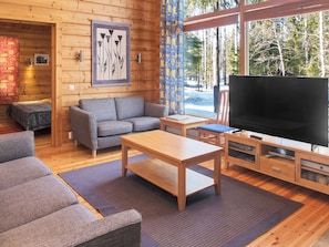 A cozy cabin interior with a sofa, a coffee table, a TV, and a window with a forest view.