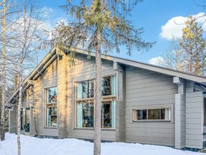 A modern house with large windows and a sloped roof, surrounded by trees and snow.