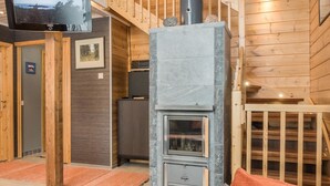 A wooden interior with a stone fireplace, a television mounted on a wooden stand, and a staircase leading to an upper level. - Pyrykieppi by Interhome (Rovaniemi)