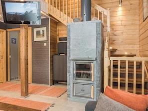 A wooden interior with a stone fireplace, a television mounted on a wooden stand, and a staircase. - Pyrykieppi by Interhome (Rovaniemi)