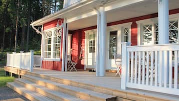 A wooden deck with a white railing, a porch with a red exterior, and a white door.