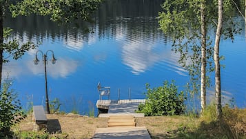 A wooden dock leading to a small boat docked at a pier, surrounded by trees and a calm lake.