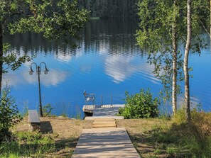 A wooden dock leading to a small boat docked at a pier, surrounded by trees and a calm lake. - Villa kukkula by Interhome (Multia)