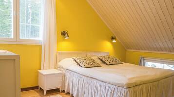 A bedroom with a sloped ceiling, a bed with floral pillows, a nightstand, and a window with curtains.