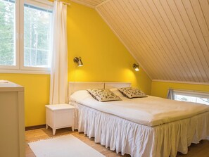 A bedroom with a sloped ceiling, a bed with floral pillows, a nightstand, and a window with curtains. - Villa kukkula by Interhome (Multia)