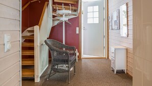 Eine Treppe mit Holzboden und weißen Geländern führt zu einer Tür. Ein Korbstuhl steht in der Nähe der Treppe, und rechts ist ein kleiner weißer Schrank zu sehen.