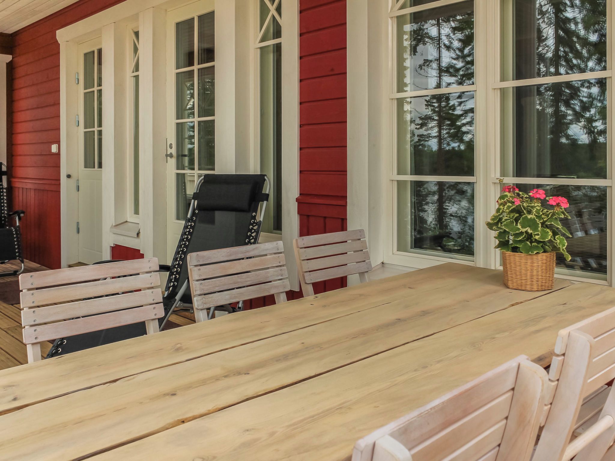 A wooden deck with a table and benches, a black chair, and a potted plant.