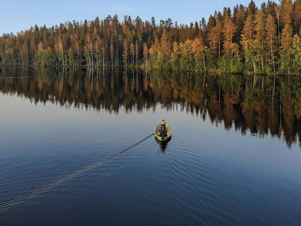 Un lago tranquilo con un bote generando ondas, rodeado por un bosque denso que se refleja en el agua.