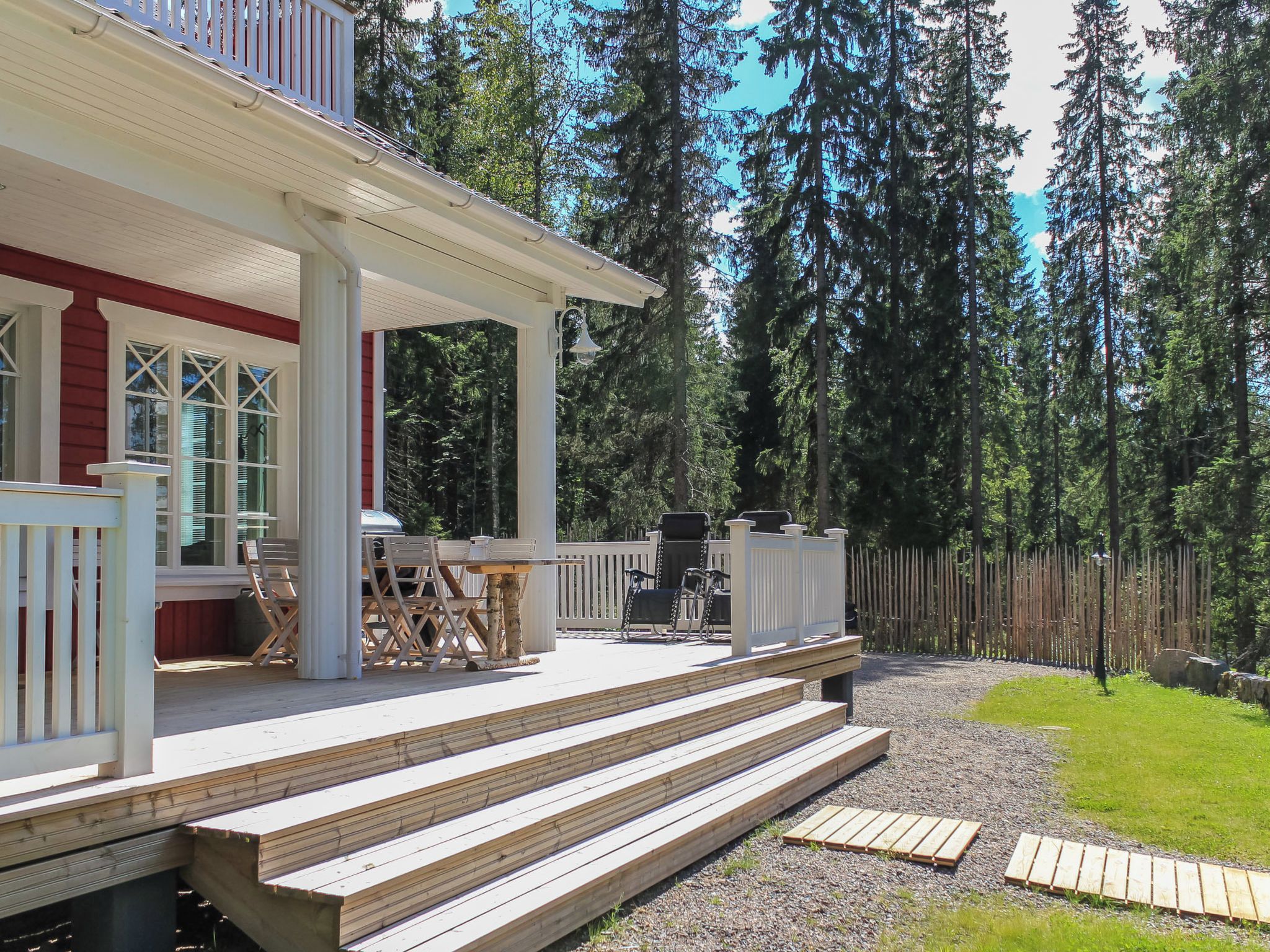 A wooden deck with outdoor furniture, a covered patio area, and a view of a forested area.