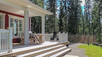 A wooden deck with outdoor furniture, a covered patio area, and a view of a forested area.
