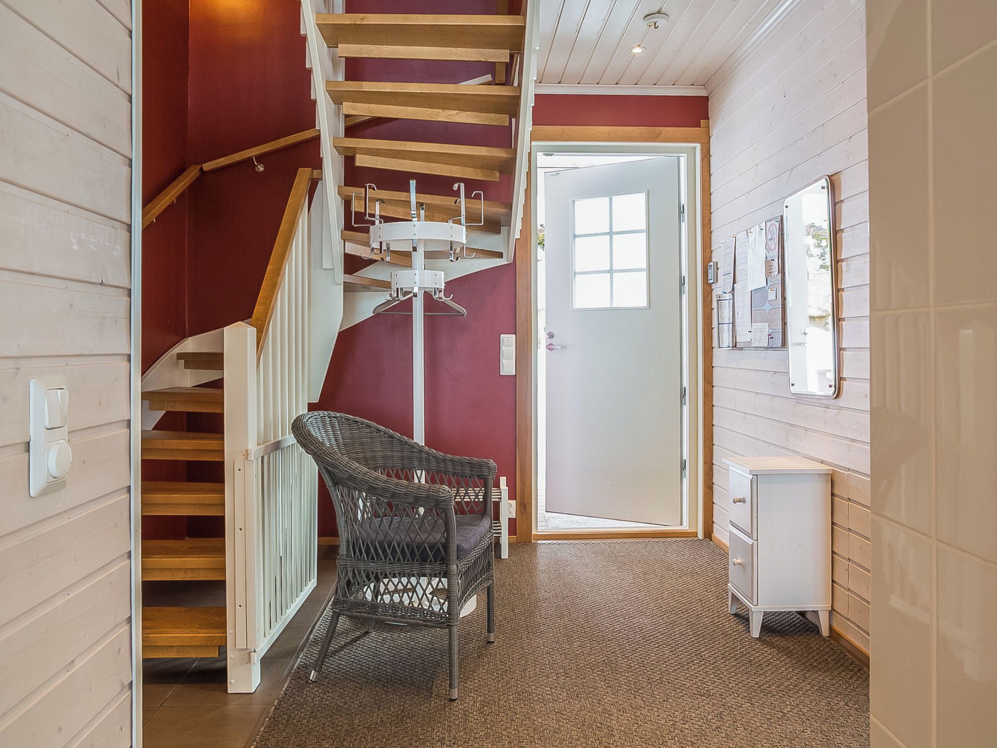 A staircase with wooden steps and a metal handrail, leading to a room with a white door and a wall-mounted bulletin board.