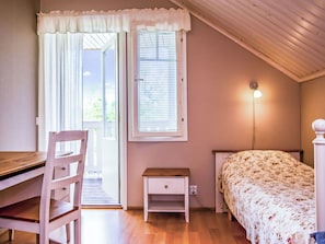 A bedroom with a bed, a desk, a chair, a nightstand, a window with blinds, and a wall-mounted light fixture. - Mielikki by Interhome (Kuopio)