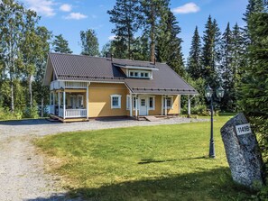 Kaksikerroksinen talo, jossa on kuisti ja sorapäällysteinen ajotie.