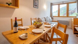 En matplats med ett träbord dukat för två personer, en flaska vin och en skål med frukt.