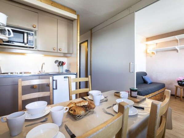 A compact kitchen with a microwave, a small refrigerator, and a dining area with a table set for breakfast.