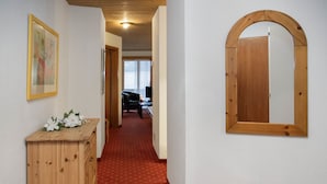 Een gang met een houten bankje, een spiegel en een deur naar een andere kamer.