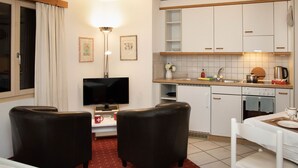 A compact hotel room with a kitchenette, a flat-screen TV, two black armchairs, a small dining table, and a red patterned carpet. - Chalet Abendrot apARTments by Interhome (Grindelwald)