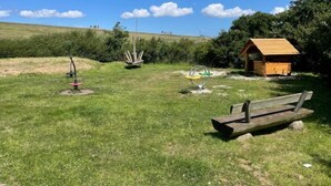 Un espace extérieur verdoyant, équipé d’appareils de musculation, d’un banc en bois et d’une petite structure en bois.