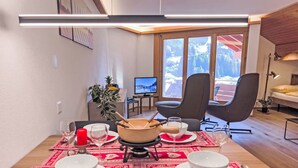 Un coin repas avec une table dressée pour quatre personnes, un téléviseur et une vue sur les montagnes grâce à de grandes fenêtres.
