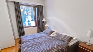 Une chambre avec deux lits, une fenêtre avec des rideaux, une table de chevet avec une lampe et un radiateur.