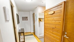 Un couloir avec une porte en bois, une petite table sur laquelle se trouve une bouteille, et un tapis sur le sol.