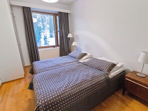 Une chambre avec deux lits, une fenêtre avec des rideaux, une table de chevet avec une lampe et un radiateur.