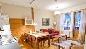 Un salon moderne comprenant un coin repas, un plancher en bois, une cuisine équipée d’une cuisinière et de grandes fenêtres avec des rideaux.