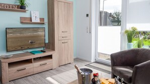 Un salon moderne avec un meuble en bois, un téléviseur à écran plat, une table à manger avec de la nourriture et des boissons, et une porte-fenêtre coulissante donnant sur un balcon.